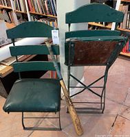 Front view of two green wooden slat-back chairs with vinyl-padded seats and Rawlings bat leaning against one