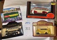 Four diecast buses in original boxes displayed on white cloth: beige and red Leyland PS1 Tiger Windover Hebble, black Guinness double-decker, yellow Chester General souvenir bus, green Hong Kong double-decker bus.