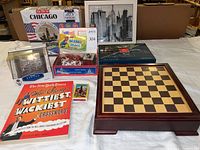 Lot overview showing all items including chess set, crossword book, cityscape puzzles, baseball figurines, and brain teaser puzzles.