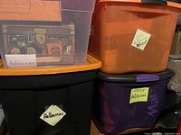 Stacked plastic storage bins labeled for Halloween decor and supplies, showing containers with orange, black, and purple lids and Halloween labels.