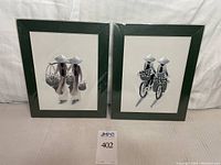 Pair of framed needlework art pieces with dark green frames showing Asian figures in silver and gray tones