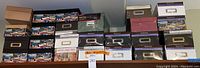 Wide view showing a large collection of storage boxes stacked and arranged on shelves. Includes several types with postcard designs, black and brown solid colors, and white labeled boxes.