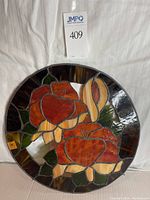 Front view of a circular stained glass disc featuring two prominent red flowers, cream-colored buds, and green leaves, bordered by dark glass pieces. The disc measures approximately 17 inches in diameter.