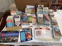 Wide view of large collection of assorted vintage and newer paper maps and travel guides from various locations.