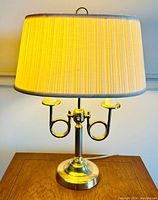 Full view of the brass Bouillotte style double table lamp with French horn shaped details and original pleated yellow lampshade with gray trim.