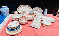 Wide view of all porcelain pieces including plates, pitchers, trays, and decorative items on red cloth