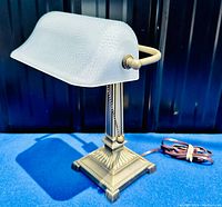 Bankers lamp side view showing metal base with detailed design, frosted stippled glass shade, and pull chain switch with brass-colored metal knobs on sides securing the shade.