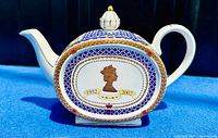 Full side view of the oval teapot showing the gold silhouette profile of Queen Elizabeth II with the dates 1952 and 2002 on a white and royal blue lattice background with red and gold accents.