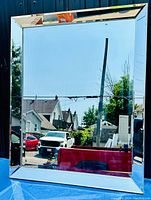 Front view of large beveled mirror reflecting outdoor scene, showcasing the entire mirror and beveled frame edges.