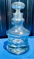 Clear crystal decanter with thick base and controlled bubble inside, photographed against a black backdrop and blue surface.