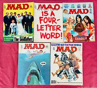 Full view of all five MAD magazines showing various parodies including The Godfather, Jaws, Star Wars, Charlie's Angels and MAD theme covers laid flat on pink surface.