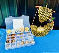 Full view of vintage coins in clear plastic organizer and decorative Viking longship on blue surface.