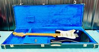 Electric guitar placed in open case showing body, neck, headstock and blue plush interior