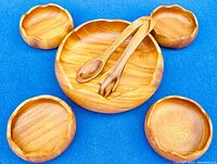 Top-down view of the set including one large teak bowl, four smaller bowls, and two serving utensils on a blue background.