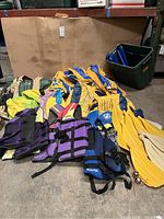 Photo of life vests, inflatable boats compressed and folded, and yellow paddles arranged on floor.