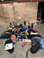Wide angle photo showing the full lot of camping and backpacking gear spread on the ground, including camping stoves, fuel cans, gaiters, water bags, and survival accessories.