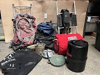 Full lot including two backpacks, two metal backpack frames, red Coleman sleeping bag, black Garcia bear canister, green Sunshower shower, aluminum canteens, and Coleman container.