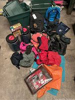 Full overview photo showing two green bear-resistant BV-500 cans, multiple backpacks, assorted stuff sacks and tarps in various colors, and a boxed cooking set.