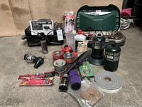 Full view of all camping gear including propane stove, grill, fuel canisters, canned heat, lantern, torch and accessories arranged on floor.