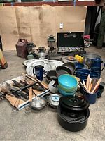 Wide view of entire lot showing all items grouped on floor, including stoves, lanterns, cookware, and utensils.