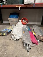 Lot items on warehouse floor including bundled poles, folded tarps, and bucket of paracord.