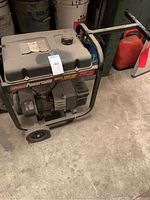 Photo of Coleman Powermate Maxa 3000 OVH generator showing full unit with frame, wheels, fuel tank, and handle.