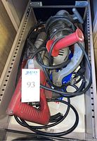 Drawer view containing four vintage corded power tools with visible cord wear and damage, plus miscellaneous blades.