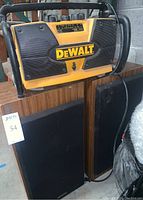 DeWalt yellow and black worksite radio/charger with rugged frame and control panel, sitting above two floor speakers with black fabric grille covers.