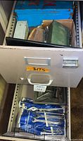 Drawer labeled 'BITS' containing various metal tools including combination wrenches in blue fabric rolls and drill bits in plastic tray.