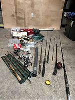 Overall view of fishing rods, reels, tackle, net, creel bag, and other gear laid out on floor.