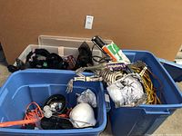 Blue plastic bins filled with Halloween decor items such as plastic skeleton, fake skulls, black lights, spiderwebs, and fake rats.