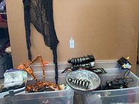 General overview of bins containing various Halloween decorations including lighting fixtures, caution tape, and black spider web fabric.