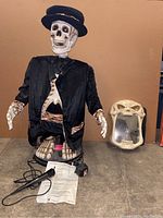Full view of animated singing Halloween skeleton figure dressed in black with microphone, skull feet, and illusion mirror beside it