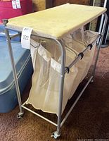 Laundry cart with stained cloth ironing board top and three mesh laundry bags shown on carpeted floor.
