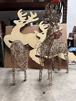Two wired metal frame animatronic reindeer with lighted noses and visible power cords, displayed on floor with painted wood reindeer silhouettes in background.