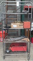 Full view of metal rolling rack with tools and boxes on shelves, showing general contents and condition.