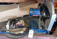 Ryobi chop saw with multiple blades and sanding discs stacked on base.