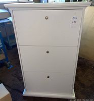 Front view of white standing shoe storage cabinet with three drop-down doors and round metal knobs.