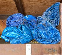 Five rolled blue tarps stacked on a wood shelf, showing dust accumulation and size variation.