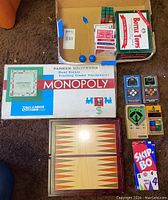 Board games and other items including Parker Brothers Monopoly game, multi-game backgammon box, Bottle Topps game, clackers, decks of cards, Rubik's Cube, and Skip-Bo game.