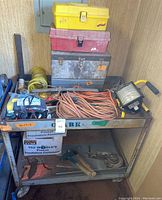 Wheeled metal cart filled with toolboxes, extension cords, work light, and various tools.