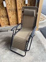 Full view of the anti gravity reclining chair in upright position showing black frame, beige fabric and pillow headrest