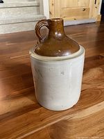 Front and side views of antique clay jug showing the beige body and brown glazed neck and handle. Chip visible on bottom edge.