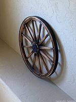 Decorative wooden wagon wheel hanging on textured wall showing its circular wooden frame, spokes, and brass stud accents.