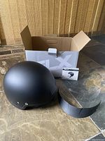 Photo showing matte black half-shell helmet next to original cardboard box and clear visor.