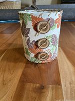 View of the lampshade's decorative exterior paper with leaf pattern, leather lacing, and wooden buttons