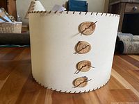 Side view of the handmade lampshade showing cream paper finish, leather lacing, and four attached aspen wood buttons with leather ties.