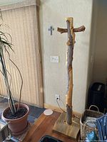 Full view of the handmade pine log coat rack positioned near a sliding door and plant, showing the natural wood texture and four pegs.