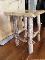 Side angle view showing the square solid pine top with natural wood grain and the sturdy log legs with supporting cross-bars.