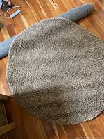 Photo showing the round brown shag rug on wooden floor, partially rolled at one end.
